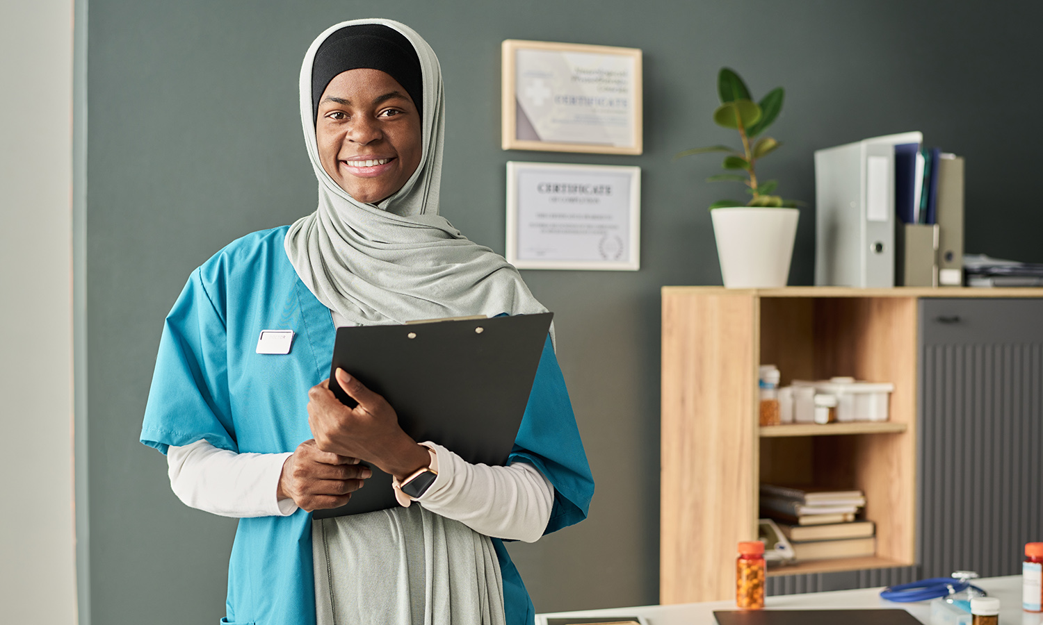nurse in office smiling at the camera holding a clipboard